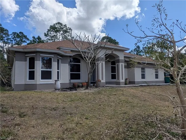View of front of property featuring stucco siding, a front yard, and roof with shingles