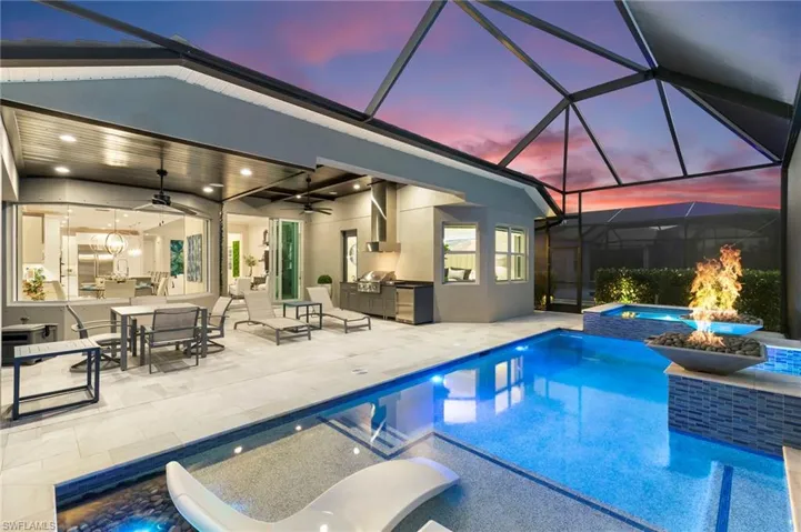 Pool at dusk featuring exterior kitchen, outdoor dining space, glass enclosure, a sunroom, and a pool with connected hot tub