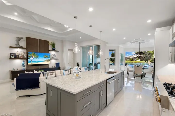 Kitchen with hanging light fixtures, light stone countertops, a kitchen bar, a large island with sink, and ornamental molding
