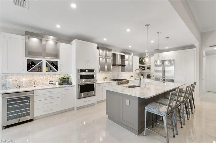 Kitchen with ornamental molding, beverage cooler, decorative light fixtures, white cabinets, and light stone countertops