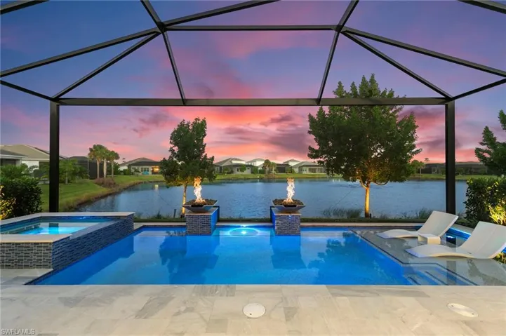 Pool at dusk with a sunroom, a lanai, a water view, and a pool with connected hot tub
