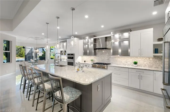 Kitchen featuring ornamental molding, white cabinetry, a breakfast bar area, decorative light fixtures, and light stone counters