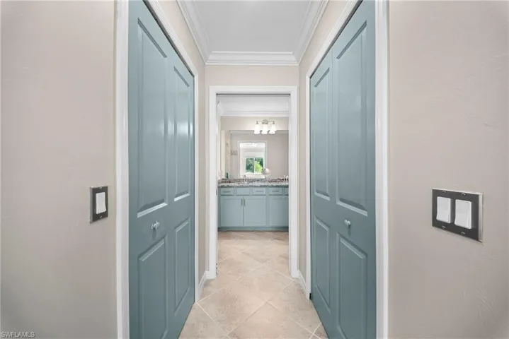Hallway featuring two-panel bifold doors with crystal knobs, crown molding, and tiled flooring
