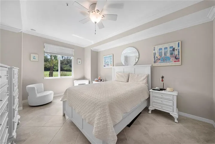 Recessed ceiling with layered crown molding, ceiling fan, large window with blinds, and tile flooring