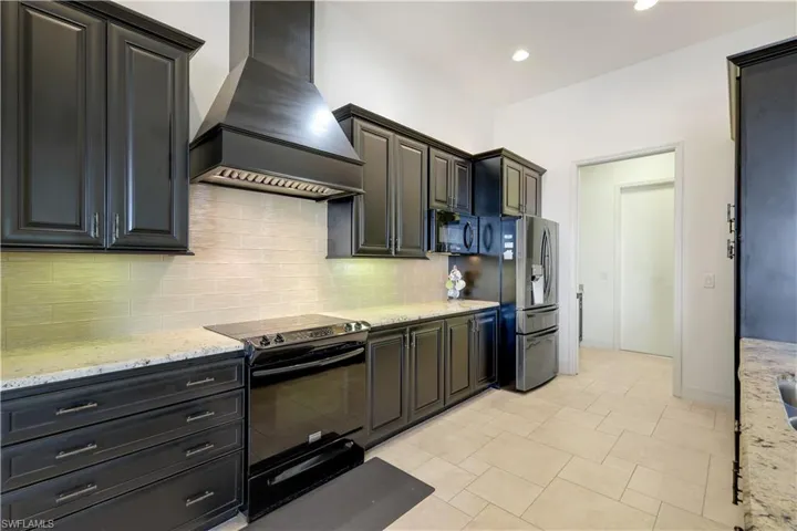 Kitchen featuring black appliances, decorative backsplash, light stone countertops, and premium range hood