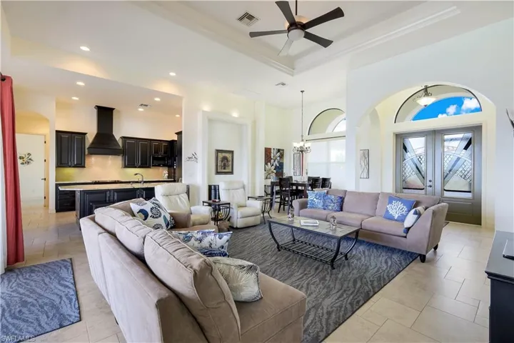 Living room with french doors, ceiling fan with notable chandelier, a raised ceiling, sink, and light tile patterned flooring