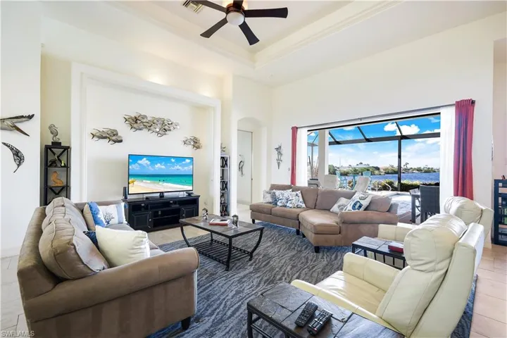 Tiled living room featuring a towering ceiling, a tray ceiling, ceiling fan, and ornamental molding