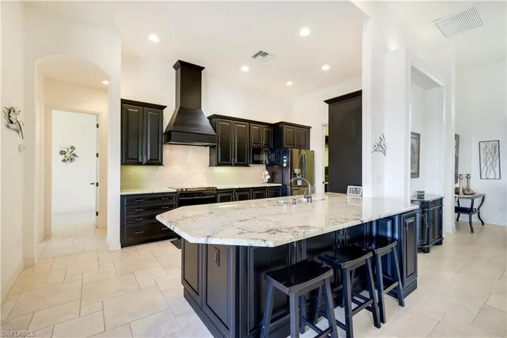 Kitchen featuring a kitchen bar, light stone countertops, tasteful backsplash, custom exhaust hood, and sink