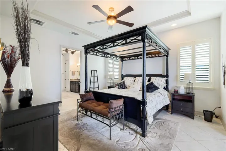 Tiled bedroom featuring connected bathroom, a raised ceiling, ceiling fan, and crown molding