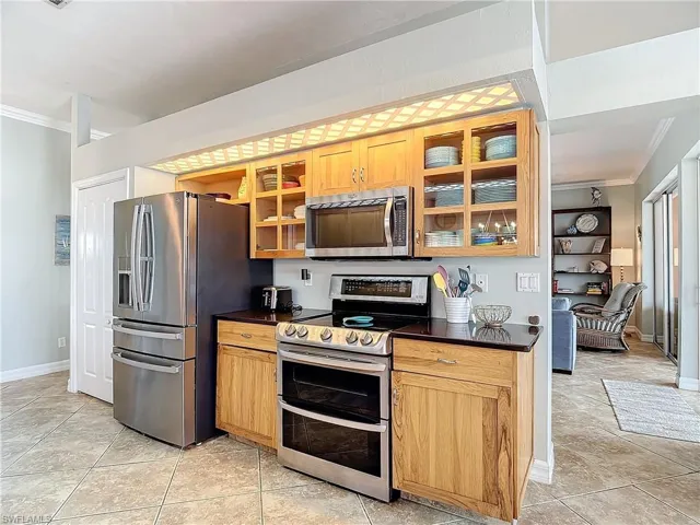 Kitchen featuring stainless steel appliances, ornamental molding, dark countertops, glass insert cabinets, and light tile patterned floors