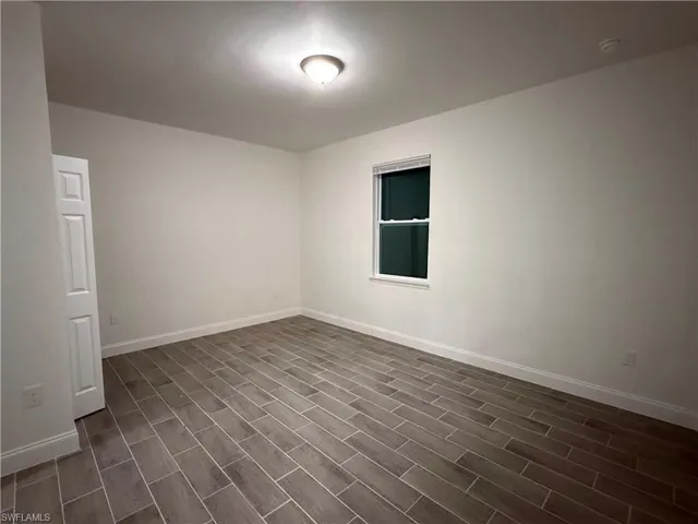 Empty room with baseboards and dark wood-type flooring