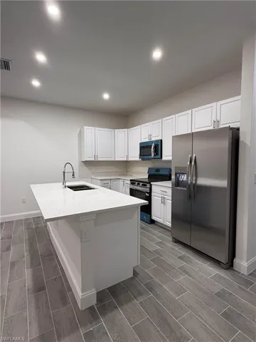 Kitchen featuring stainless steel appliances, wood tiled floors, white cabinetry, recessed lighting, and light stone counters