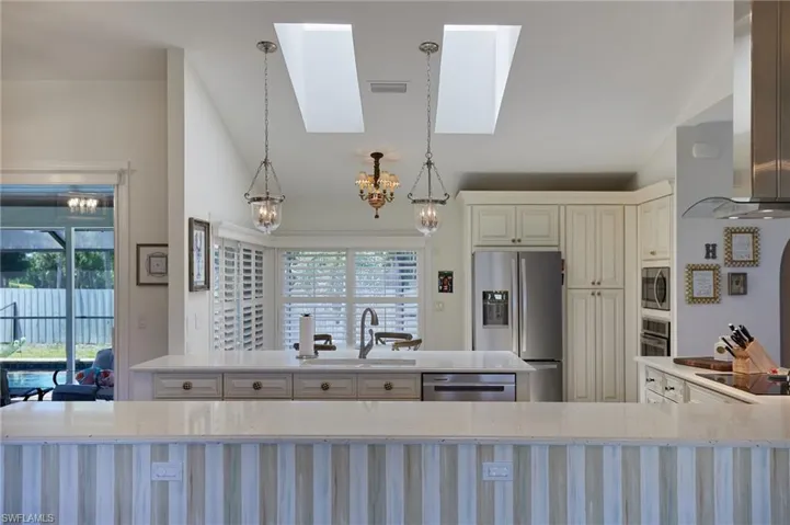 Kitchen featuring a sink, island exhaust hood, stainless steel appliances, and vaulted ceiling with skylight