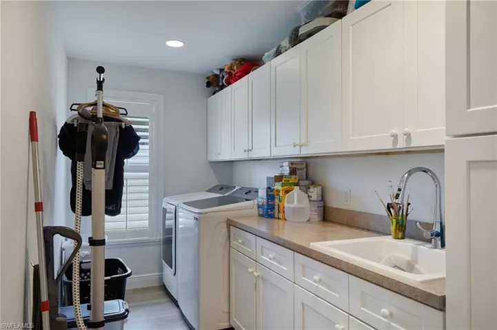 Laundry area featuring washer and clothes dryer, a sink, cabinet space, light wood-type flooring, and baseboards