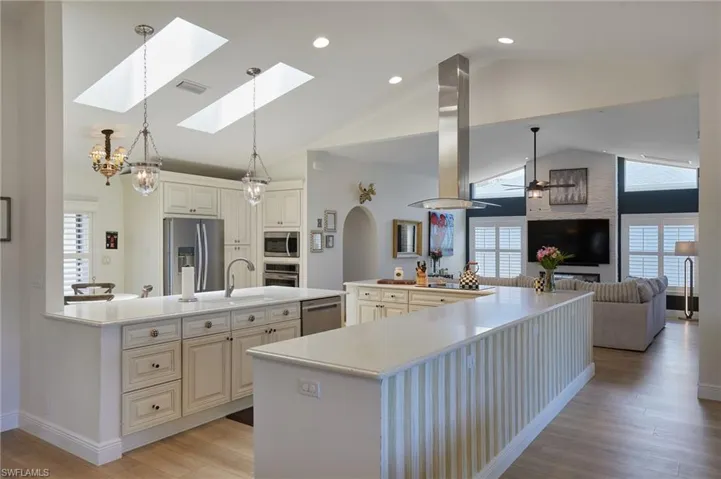 Kitchen with stainless steel appliances, island exhaust hood, a large island with sink, high vaulted ceiling, and light countertops