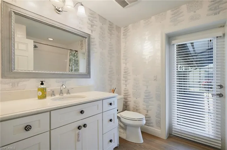 Bathroom with wallpapered walls, toilet, vanity, and wood like finished floors