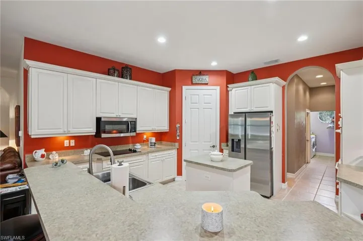 Kitchen featuring arched walkways, white cabinets, stainless steel appliances, a kitchen island, and recessed lighting