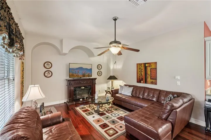 Living room with a ceiling fan, dark wood-style flooring, and a glass covered fireplace