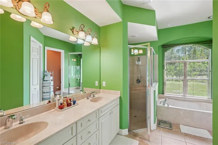 Bathroom featuring a bath, a stall shower, double vanity, and light tile patterned floors