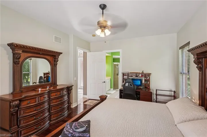 Bedroom featuring dark wood-type flooring, multiple windows, ceiling fan, and connected bathroom