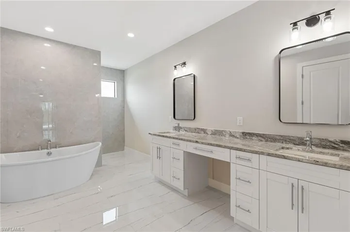 Bathroom featuring dual vanity, a washtub, tile flooring, and tile walls