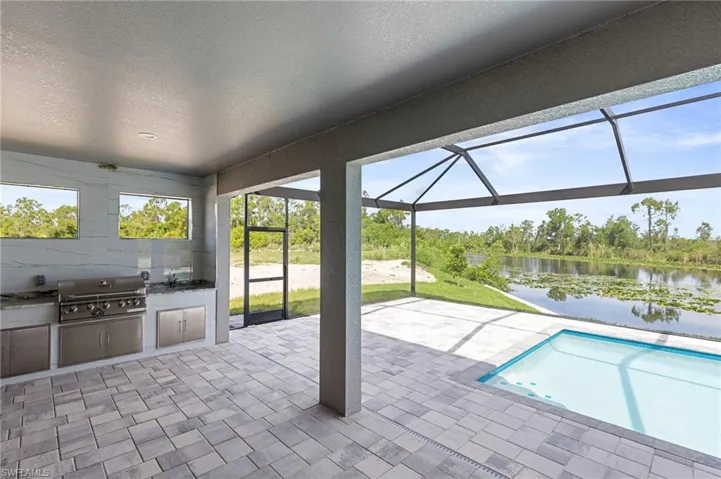 View of swimming pool with a patio, exterior kitchen, a water view, grilling area, and glass enclosure