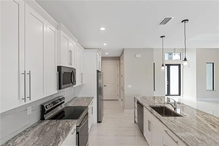 Kitchen with white cabinets, appliances with stainless steel finishes, light stone countertops, and pendant lighting
