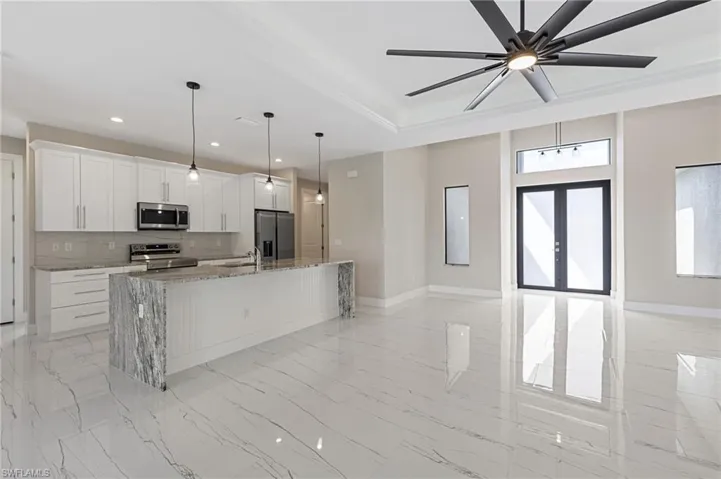 Kitchen featuring stainless steel appliances, white cabinets, light tile floors, and a kitchen island with sink