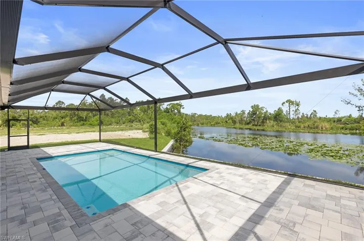 View of pool with a water view, glass enclosure, and a patio area