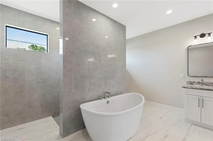 Bathroom featuring tile walls, tile flooring, vanity, and a bath to relax in