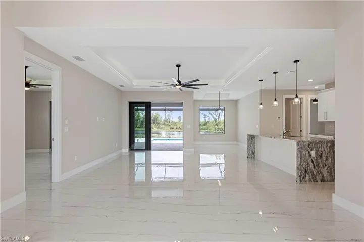 Unfurnished living room featuring sink, ceiling fan, light tile floors, and a raised ceiling