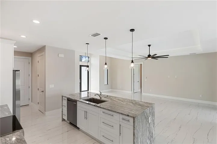 Kitchen with ceiling fan, a tray ceiling, dishwasher, sink, and white cabinets