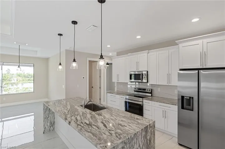 Kitchen featuring tasteful backsplash, stainless steel appliances, sink, a kitchen island with sink, and white cabinetry
