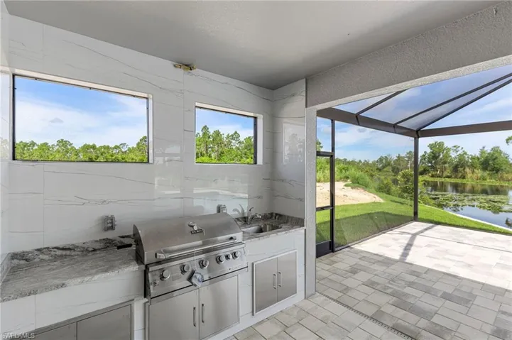 Kitchen with a water view, tile walls, light stone countertops, sink, and light tile floors