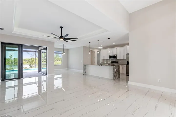 Unfurnished living room with ceiling fan, sink, light tile flooring, and a tray ceiling