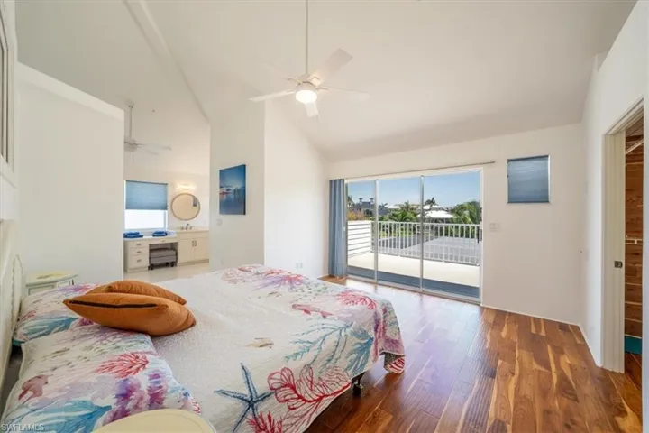 Bedroom featuring access to outside, high vaulted ceiling, wood finished floors, ceiling fan, and connected bathroom