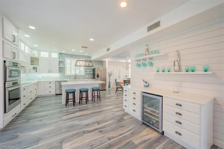 Kitchen featuring beverage cooler, stainless steel appliances, a breakfast bar, open shelves, and recessed lighting
