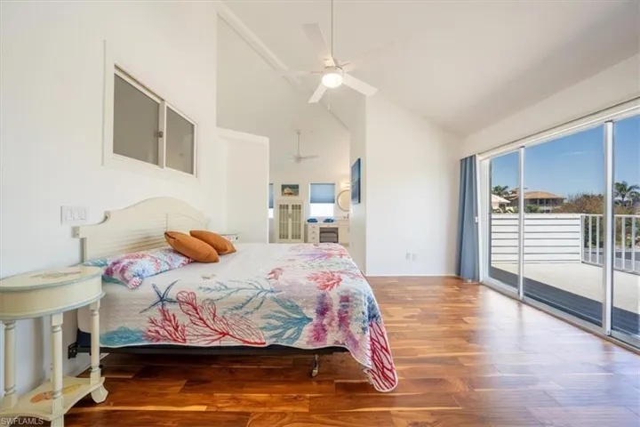 Bedroom with access to exterior, high vaulted ceiling, wood finished floors, and a ceiling fan