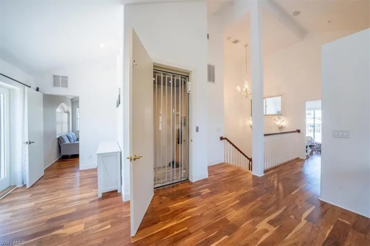 Hall with high vaulted ceiling, wood finished floors, an upstairs landing, and a chandelier