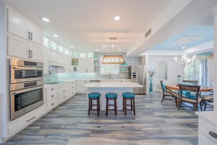 Kitchen featuring stainless steel appliances, a chandelier, white cabinetry, light countertops, and decorative backsplash