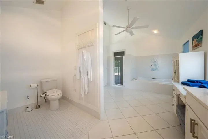 Bathroom featuring toilet, a vanity, a bath, and tile flooring