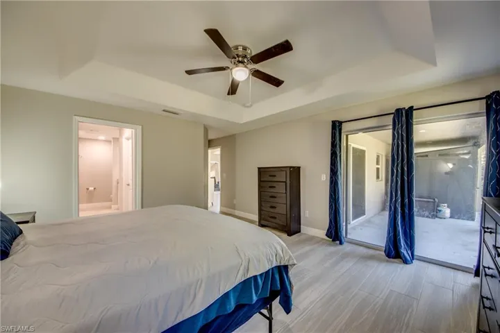 Bedroom with a raised ceiling, access to outside, a ceiling fan, ensuite bath, and light wood-style flooring