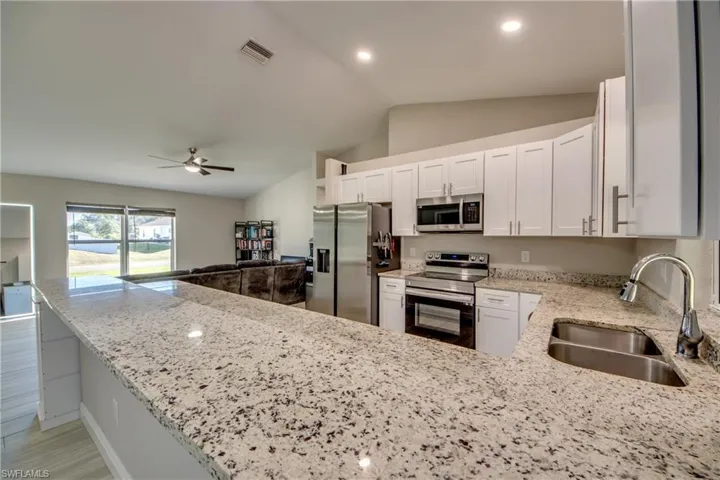 Kitchen with stainless steel appliances, light stone countertops, open floor plan, white cabinets, and lofted ceiling