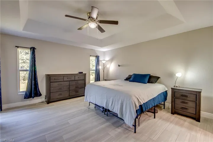Bedroom with a raised ceiling, ceiling fan, and wood finish floors