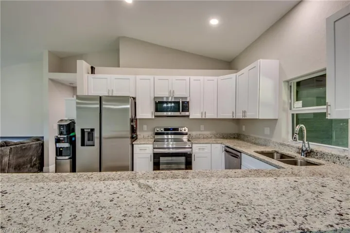 Kitchen with light stone countertops, stainless steel appliances, white cabinets, and vaulted ceiling