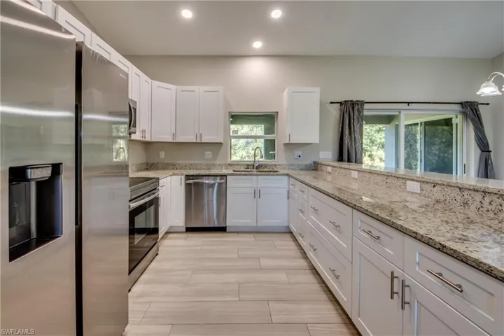 Kitchen featuring appliances with stainless steel finishes, white cabinets, light stone countertops, recessed lighting, and plenty of natural light
