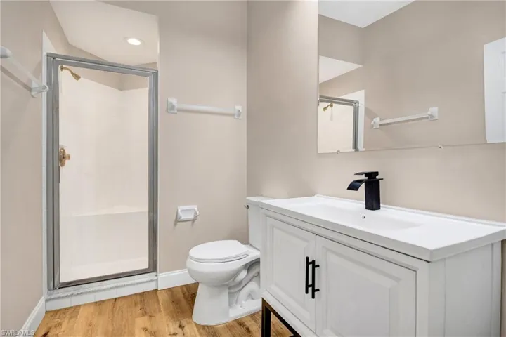 Full bathroom featuring toilet, wood finished floors, a stall shower, vanity, and baseboards