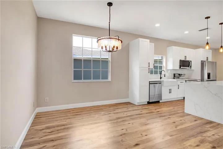 Kitchen featuring light wood-style floors, baseboards, a chandelier, appliances with stainless steel finishes, and white cabinetry