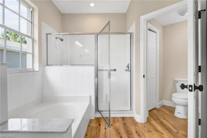 Full bath featuring a shower stall, a garden tub, toilet, and wood finished floors