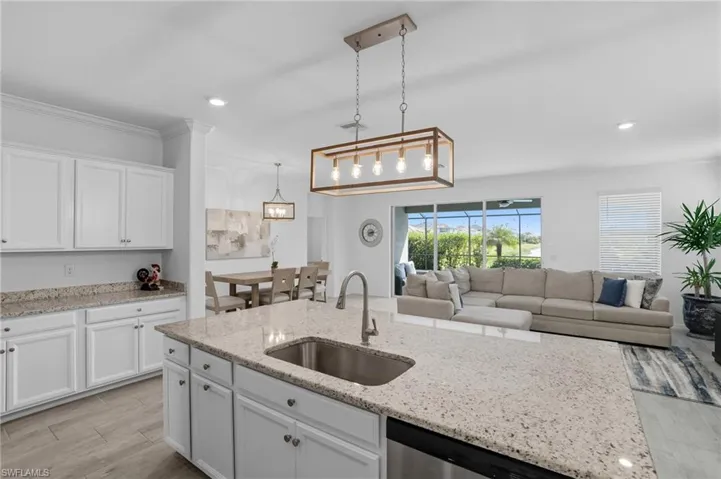 Kitchen with white cabinets, light wood-style flooring, light stone countertops, decorative light fixtures, and recessed lighting